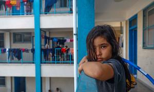 An eight-year-old girl, watches other children play in UNRWA school playground. "I want to play with them but I am afraid to leave the room. I don’t know how they can play without being scared, I just want to go back home", she said.