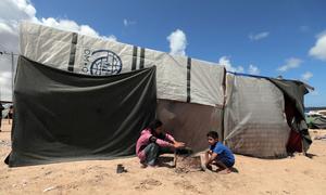 Two children play outside a shelter in Gaza fashioned from material including from the UN.