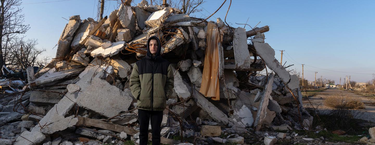 A teenage boy stands in front of a destroyed school in the village of Partyzanske close to the frontline.
