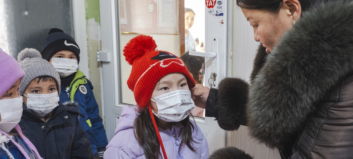 A kindergarten teacher helps a child with a face mask before outdoor activities in Nalaikh, Mongolia.
